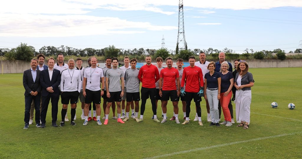 Spieler, Trainerstab sowie Vertreter:innen von KADA, younion und dem AMS posieren fpr ein Gruppenfoto auf dem Spielfeld des Sport VIVA Landessportzentrums